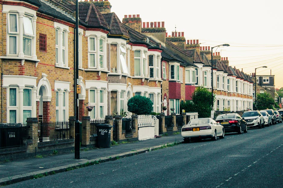 Photograph of a residential street in Walthamstow village showing a row of traditional brick terraced houses with white bay windows and pitched roofs, each house having a small front garden enclosed b